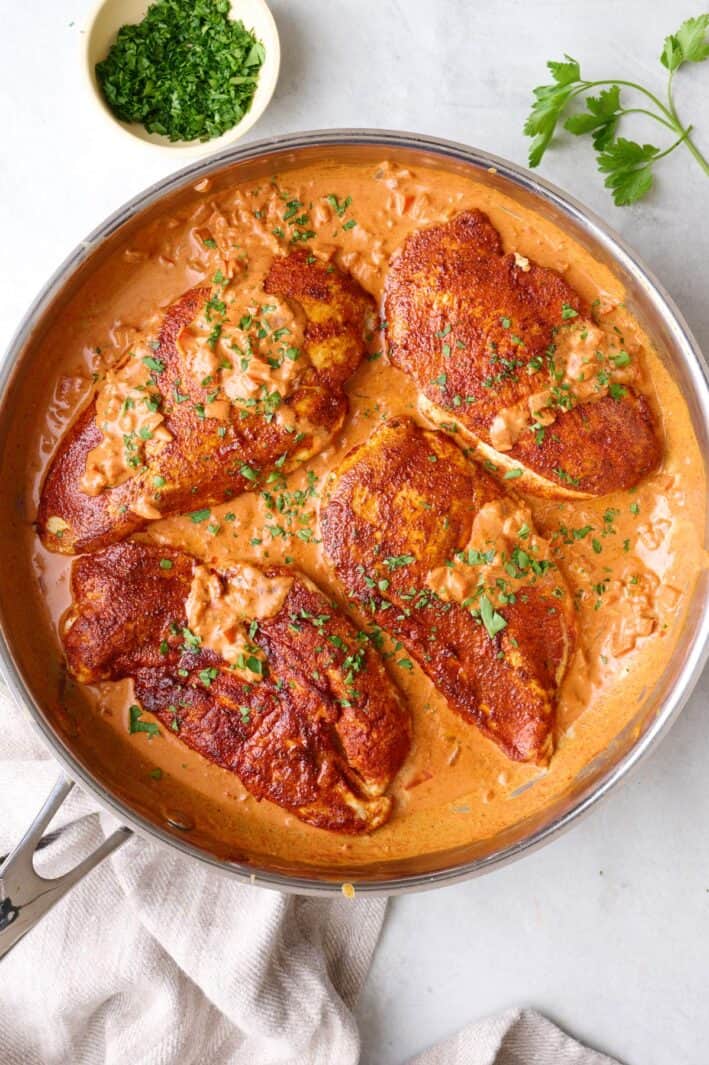 Creamy cajun chicken in the skillet with cream sauce, lightly drizzled over chicken.