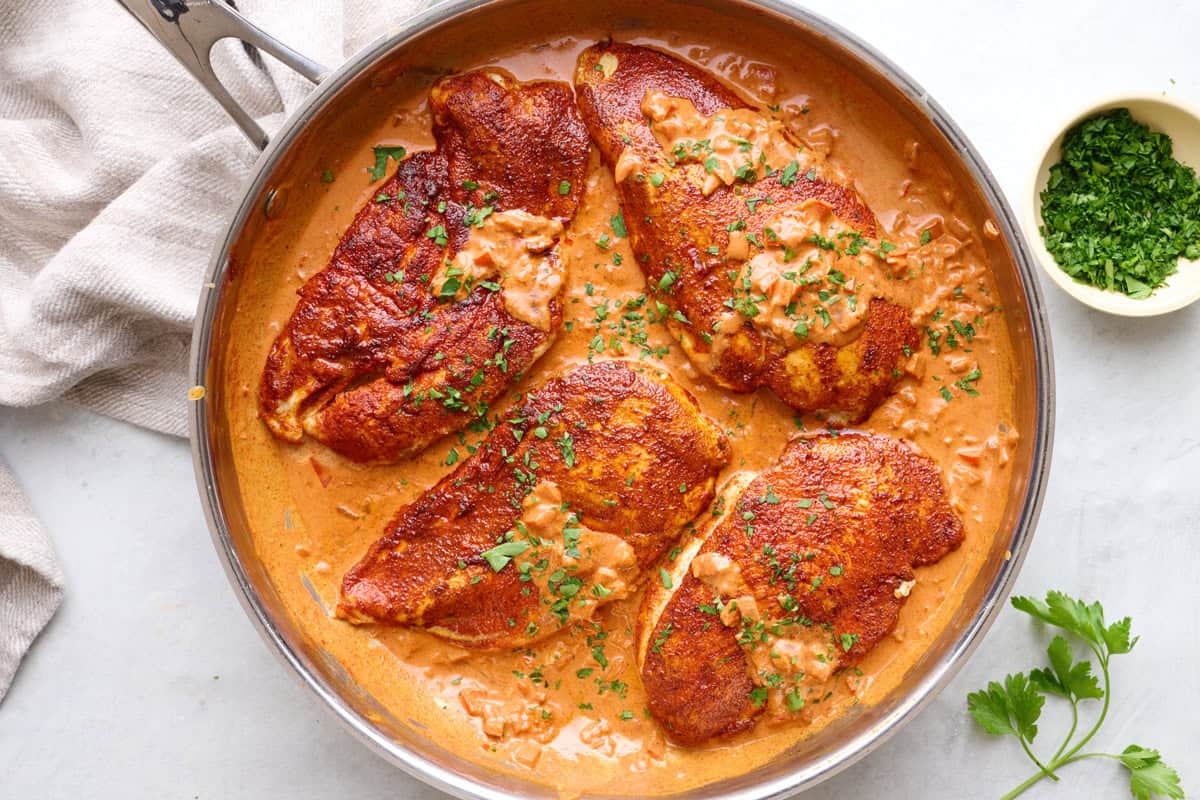 Creamy cajun chicken in the skillet with cream sauce, lightly drizzled over chicken.