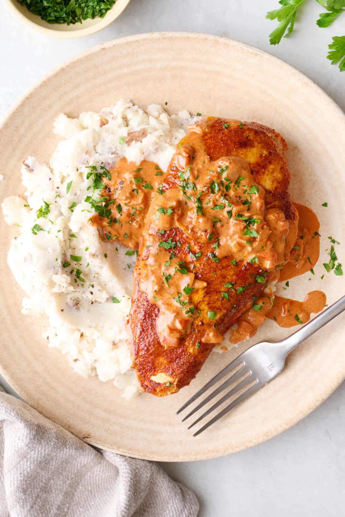 Serving of creamy cajun chicken served with mashed potatoes, with sauce drizzled on top, fork resting on plate.