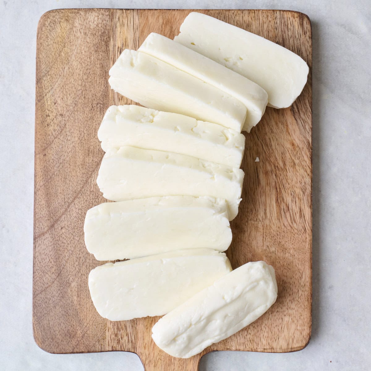 Drained halloumi on cutting board cut into thin wide pieces.