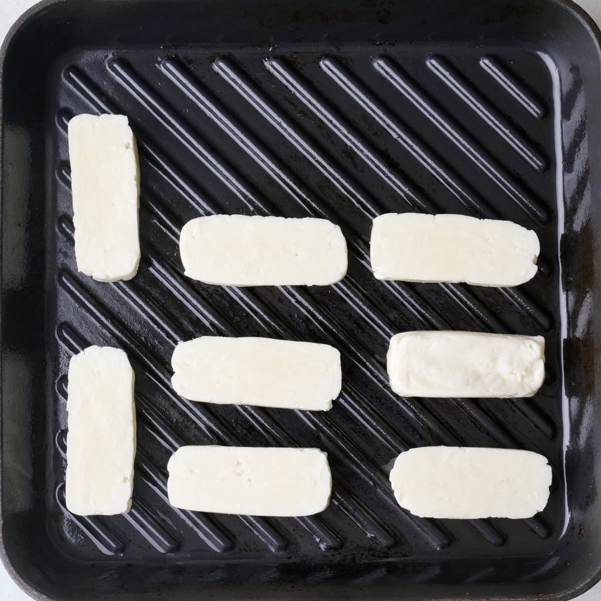 Sliced halloumi in a single layer on oiled grill pan.