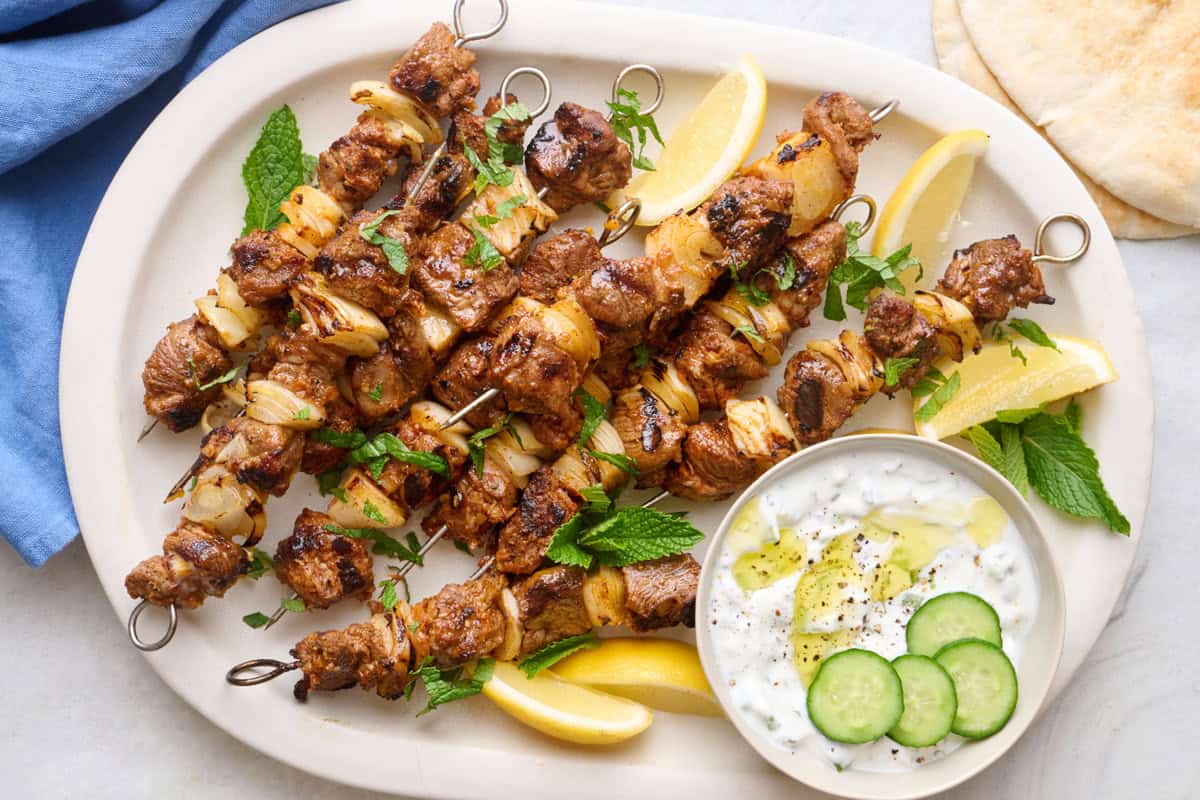 Grilled lamb kabobs on a platter with yogurt sauce for dipping.