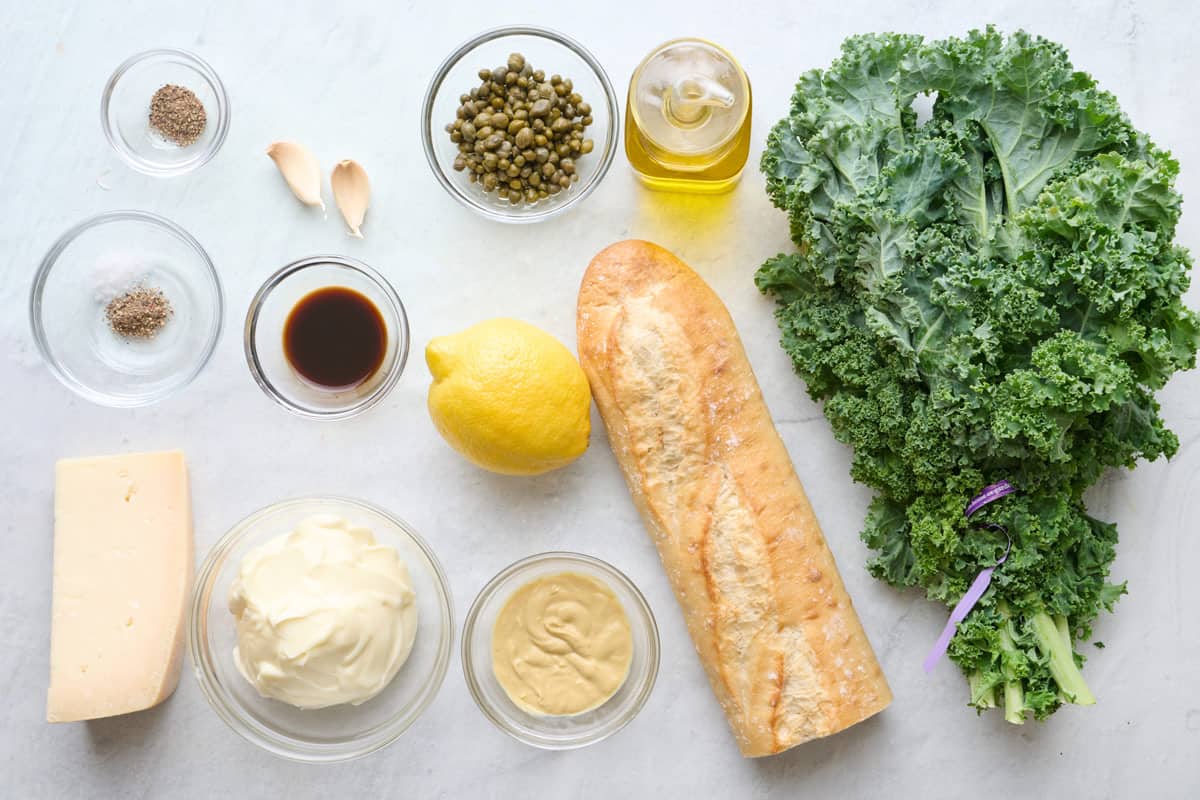 Ingredients for recipe: salt, pepper, garlic, Worcestershire sauce, parmesan, mayonnaise, lemon, Dijon mustard, capers, oil, baguette, and kale.