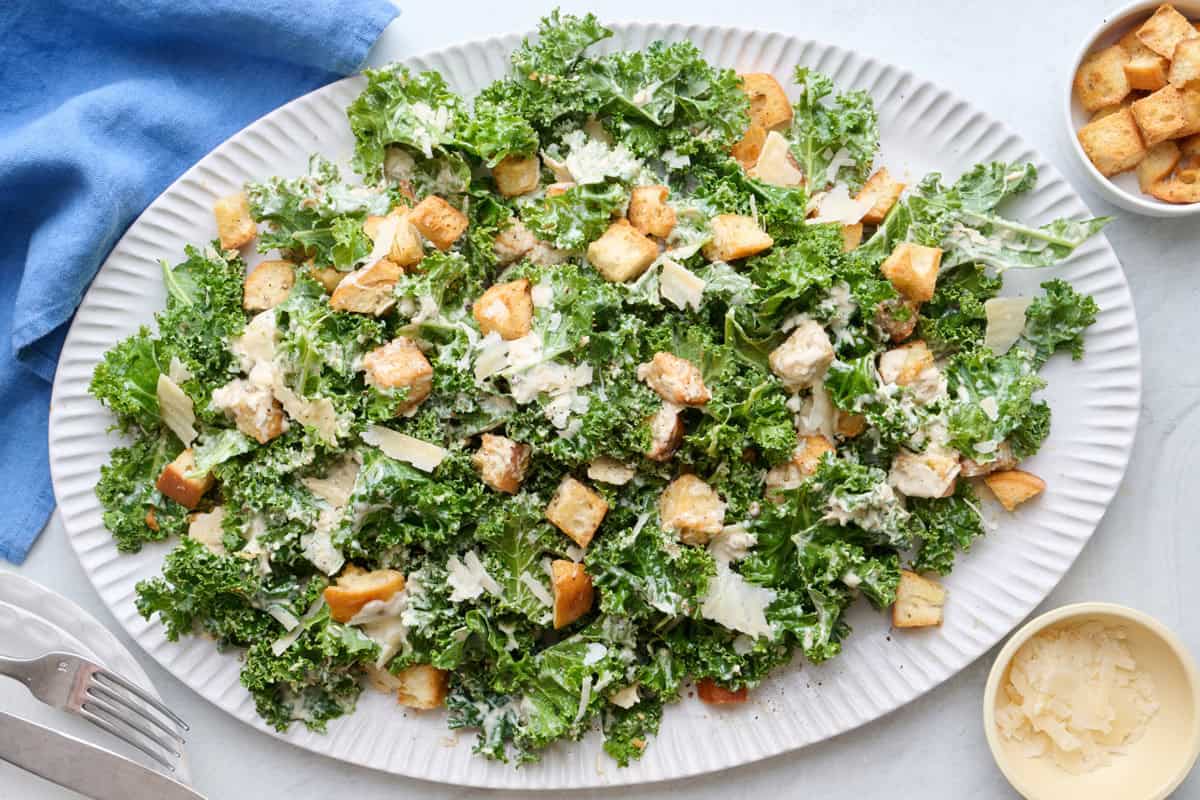 Tossed kale caesar salad on a serving platter with extra shaved parmesan and croutons on top.