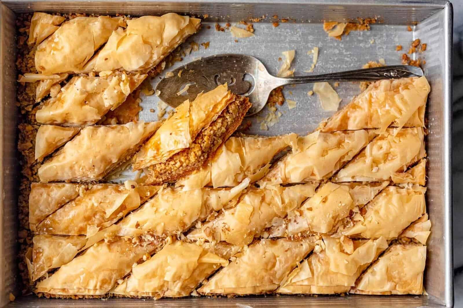 Baklava in a tray after cooled and cut into with spatula in tray