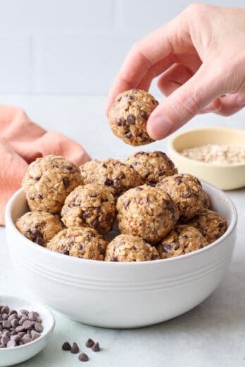 No bake energy bites in a bowl with a hand lifting one up.