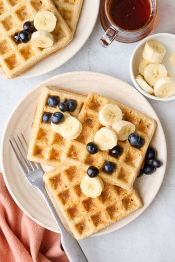 Easy oatmeal waffles on a plate with fresh blueberries and sliced bananas on top.