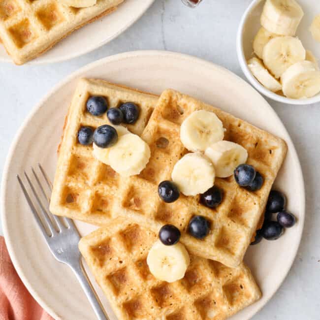 Easy oatmeal waffles on a plate with fresh blueberries and sliced bananas on top.