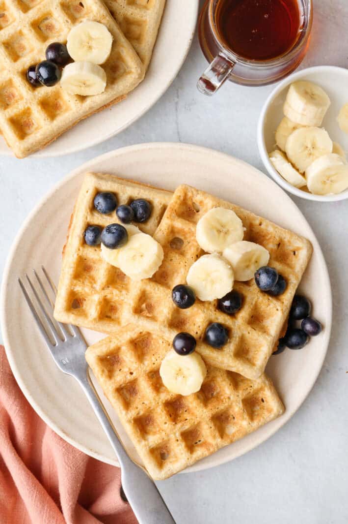 Easy oatmeal waffles on a plate with fresh blueberries and sliced bananas on top.
