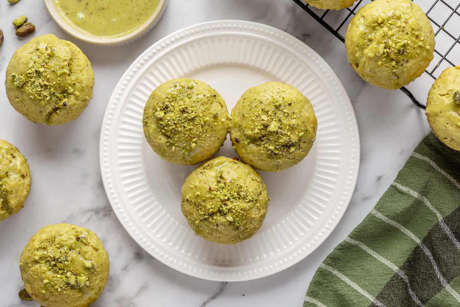 Pistachio muffins on a white plate and wire cooling rack.