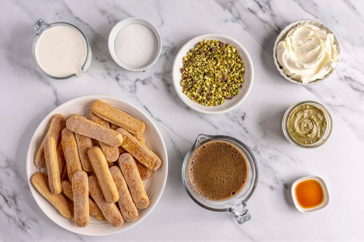 Ingredients for recipe: heavy cream, sugar, lady fingers, chopped pistachios, espresso, mascarpone cheese, pistachio butter, and vanilla.