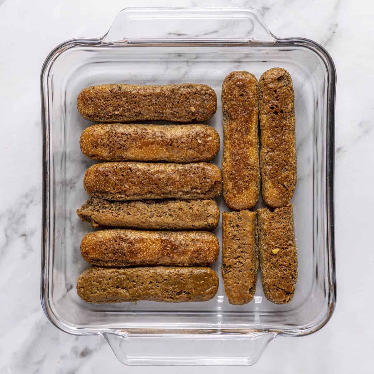 Espresso soaked lady fingers layering bottom of an 8-inch square dish.