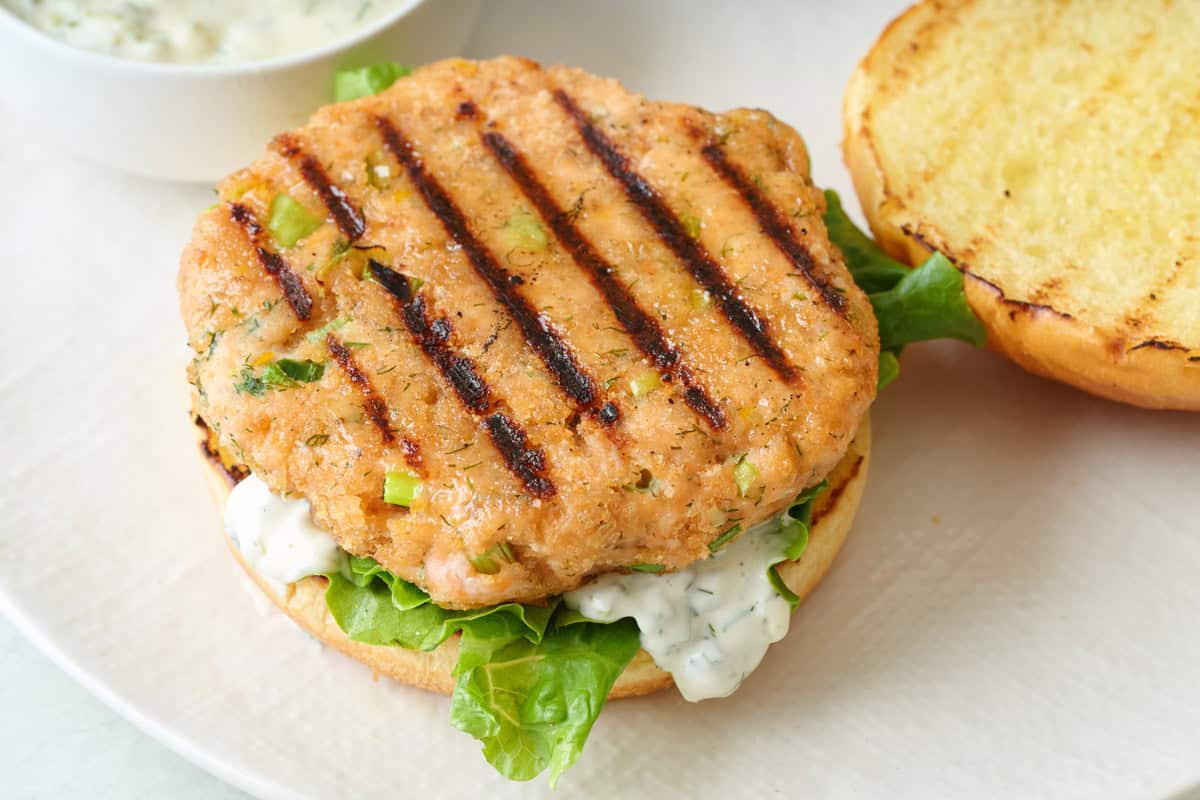 Grilled salmon burger patty on a bun with lettuce and tartar sauce.