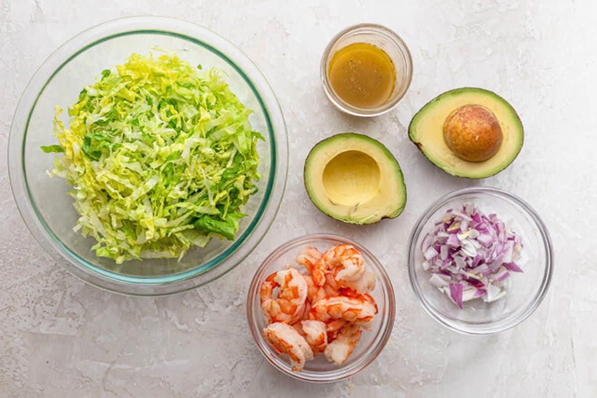 Ingredients for recipe: shredded lettuce, avocado, cooked shrimp, dressing, and red onions.