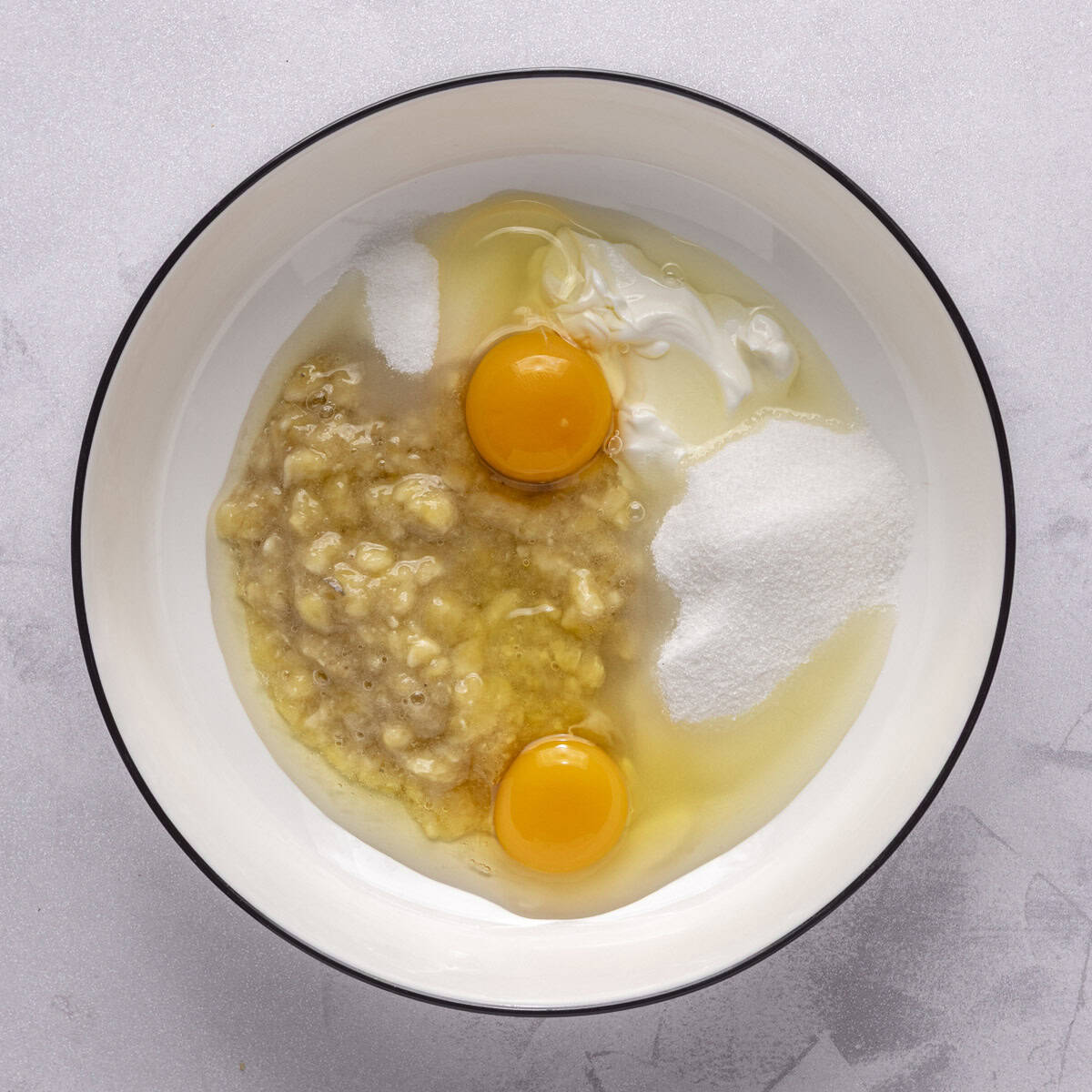 Mashed bananas, eggs, sugar, and yogurt in a bowl.