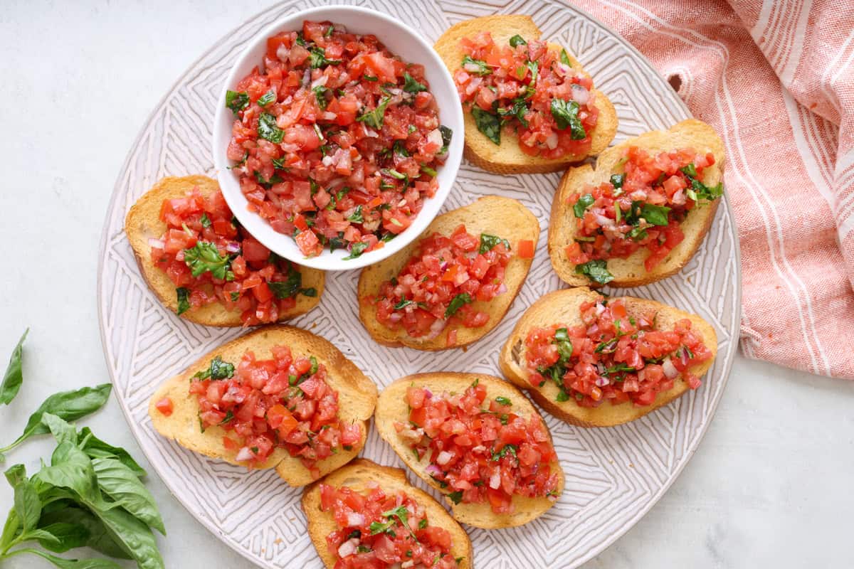 Tomato basil bruschetta on a plate with extra tomato mixture.
