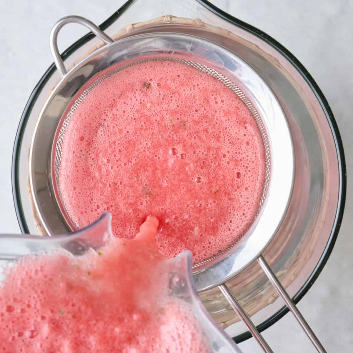 Juice poured over a fine mesh strainer into pitcher.