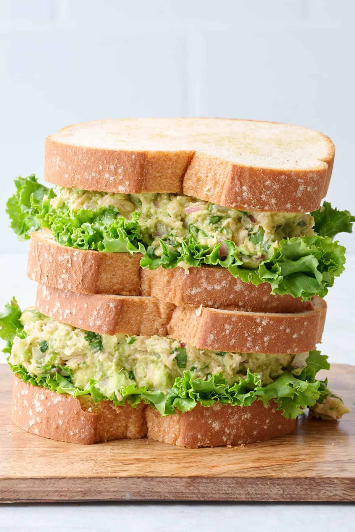 Two avocado sandwiches on lightly toasted bread with leafy lettuce and stacked up.