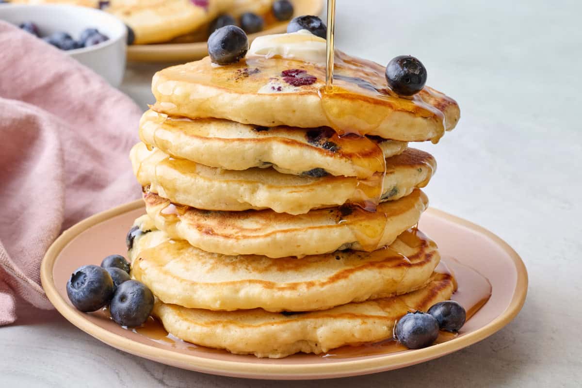 Easy homemade blueberry pancakes on a plate with maple syrup being poured on top.