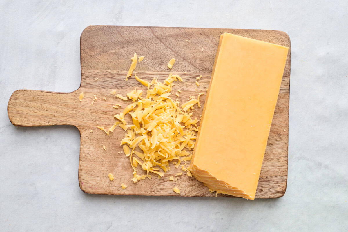 Ingredient for recipe: block yellow cheddar cheese on a small cutting board with some shredded.