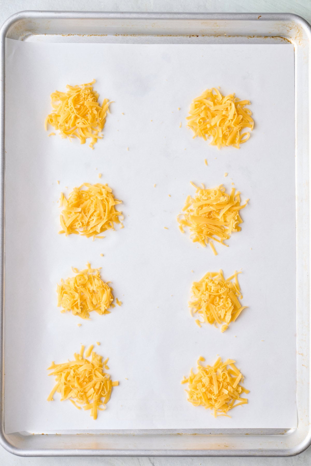 Shredded cheese circles on a parchment lined baking sheet before baking.