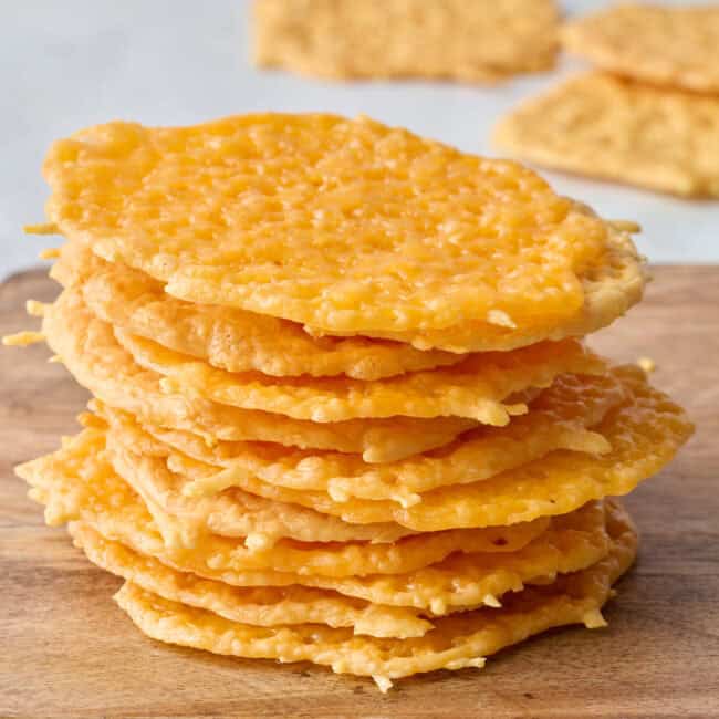 Cheese crisps stacked up with a few extra scattered in background.