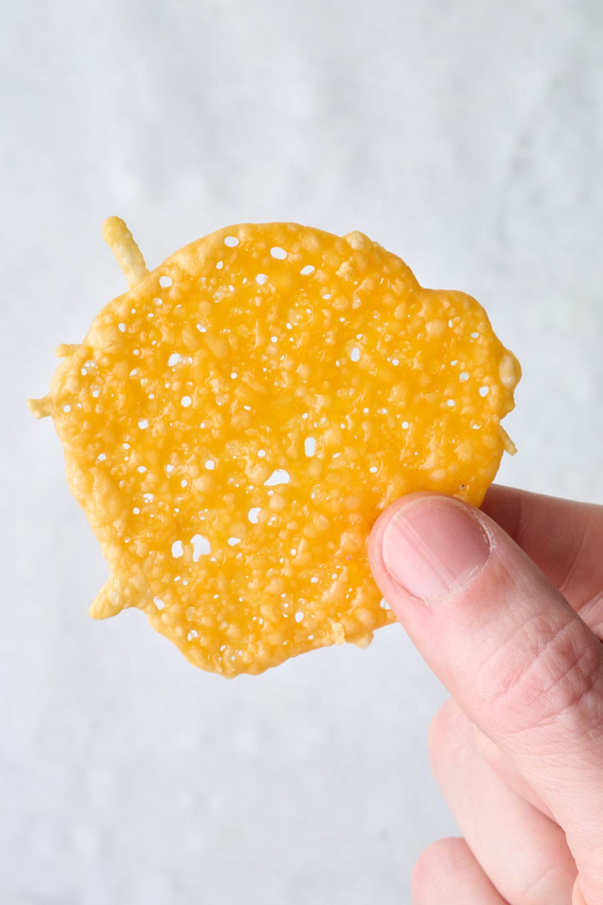 Hand holding up a cheese crisp.