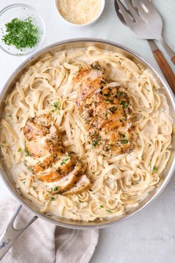 Chicken Fettuccine alfredo pasta in skillet tossed in sauce with sliced chicken slightly fanned out on top