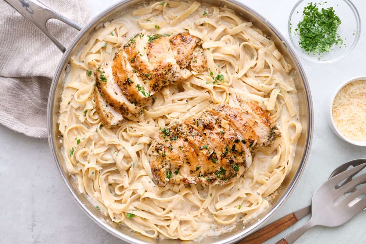 Fettuccine alfredo pasta in skillet tossed in sauce with sliced chicken slightly fanned out on top.