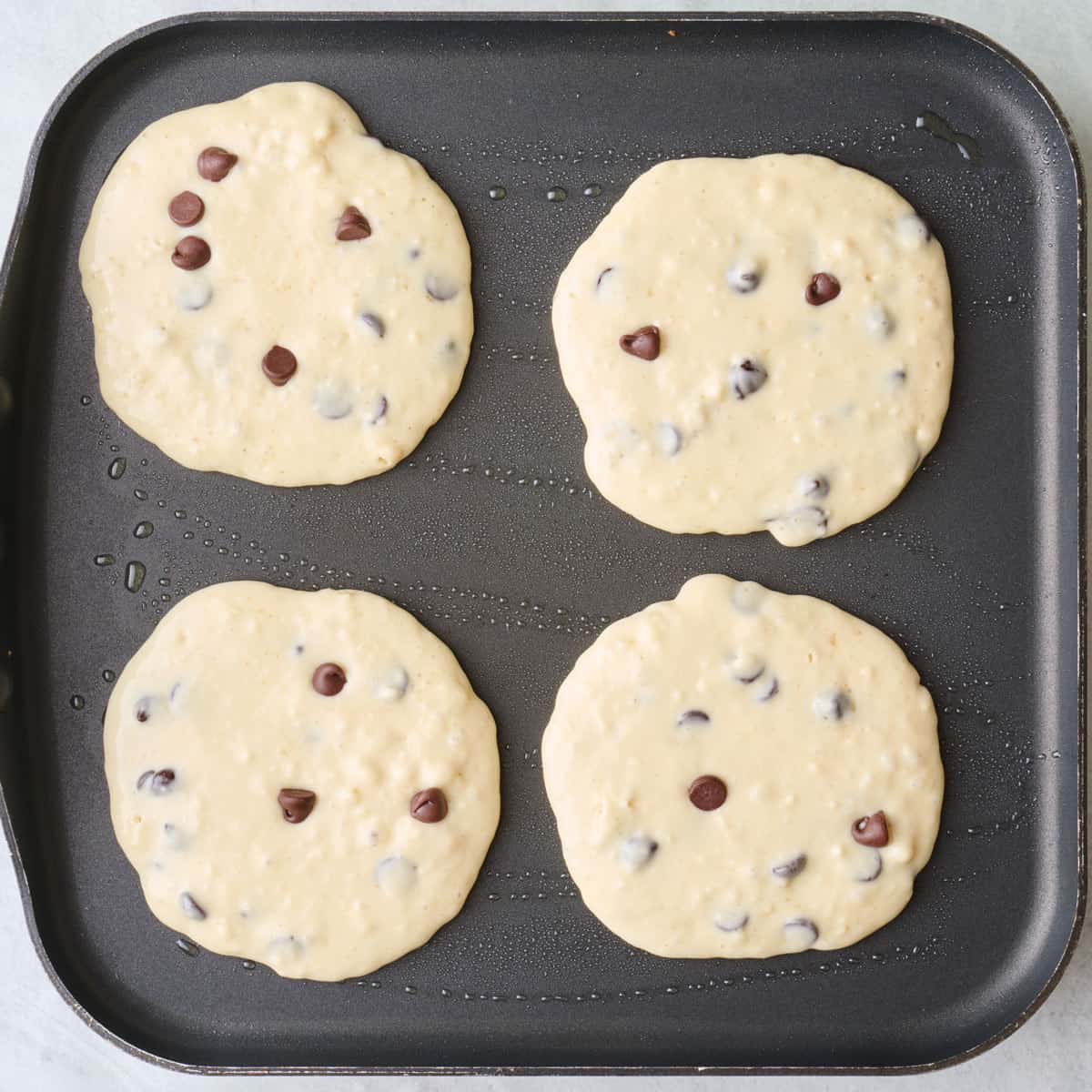 Four pancakes on a griddle before cooking.