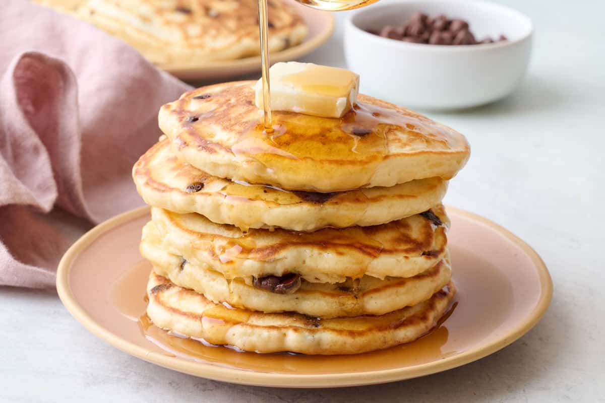 Plate of homemade chocolate chip pancakes stacked up with maple syrup being poured on top.