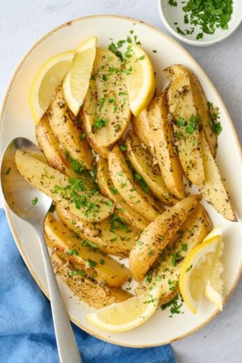 Greek lemon potato wedges on a plater with fresh lemon and parsley.