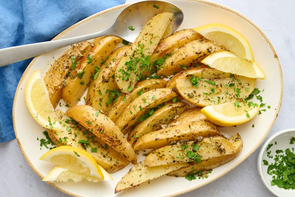 Greek lemon potato wedges on a plater with fresh lemon and parsley.