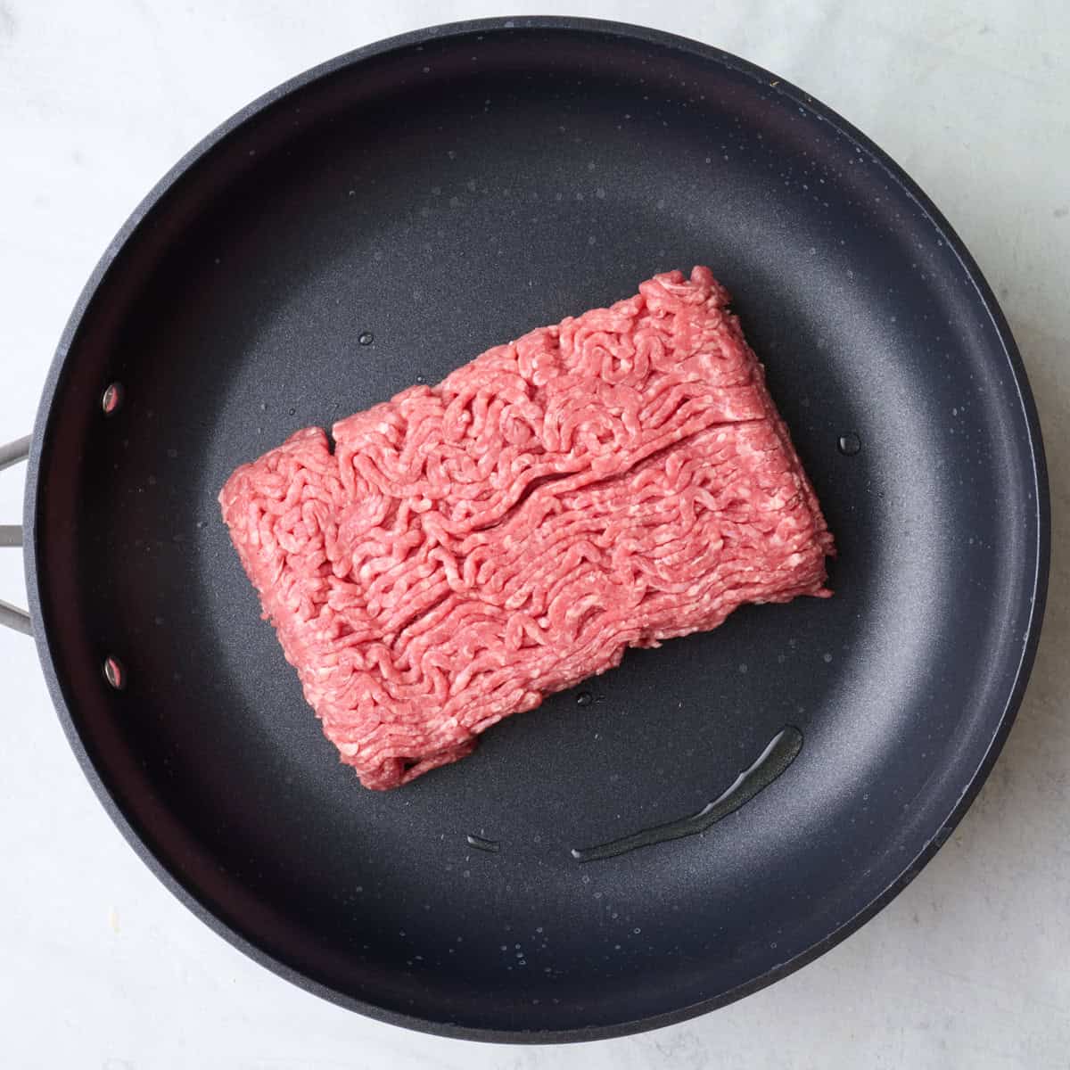 Ground beef in a skillet before cooking.