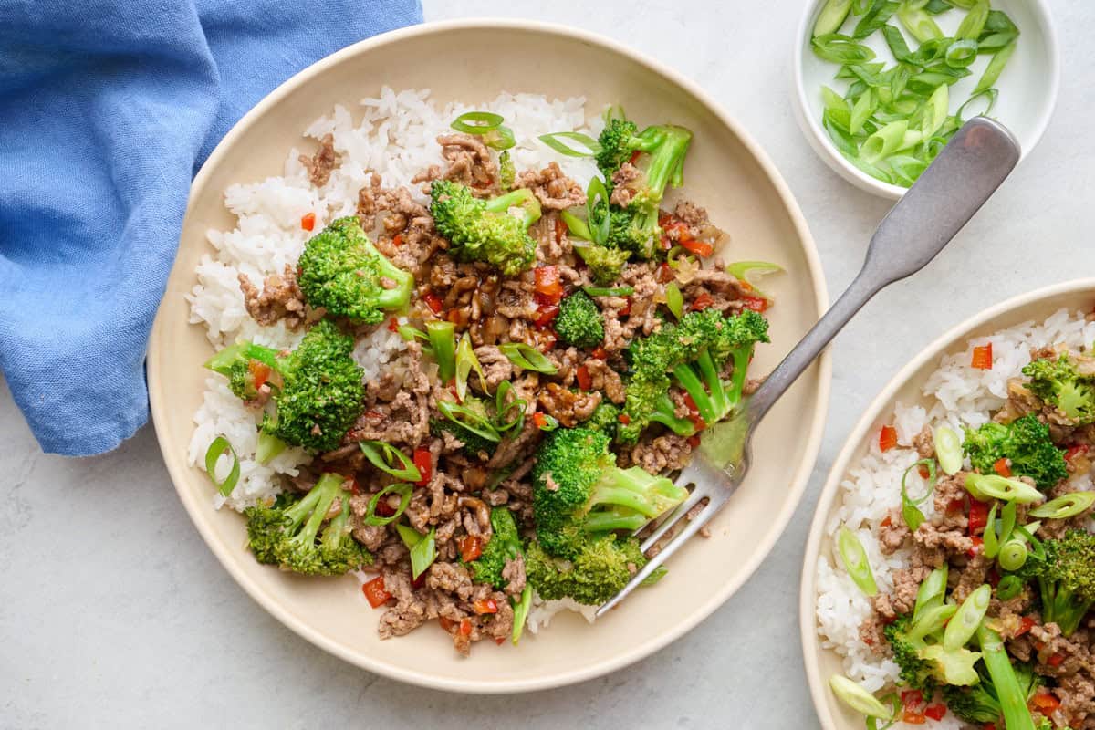 Two servings of Beef stir fry served over rice in shallow bowls topped with green onions.
