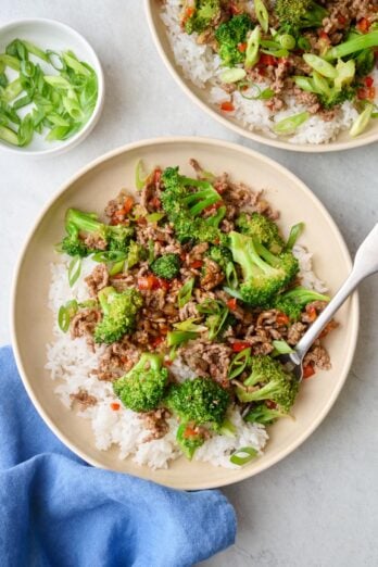Two servings of Beef stir fry served over rice in shallow bowls topped with green onions.