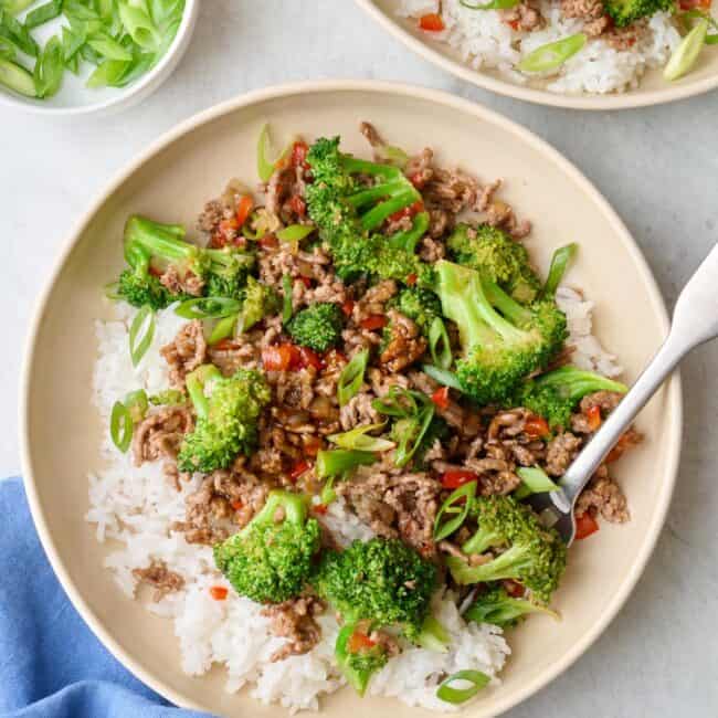 Two servings of Beef stir fry served over rice in shallow bowls topped with green onions.
