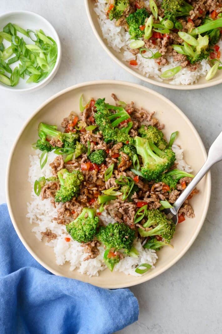 Two servings of Beef stir fry served over rice in shallow bowls topped with green onions.