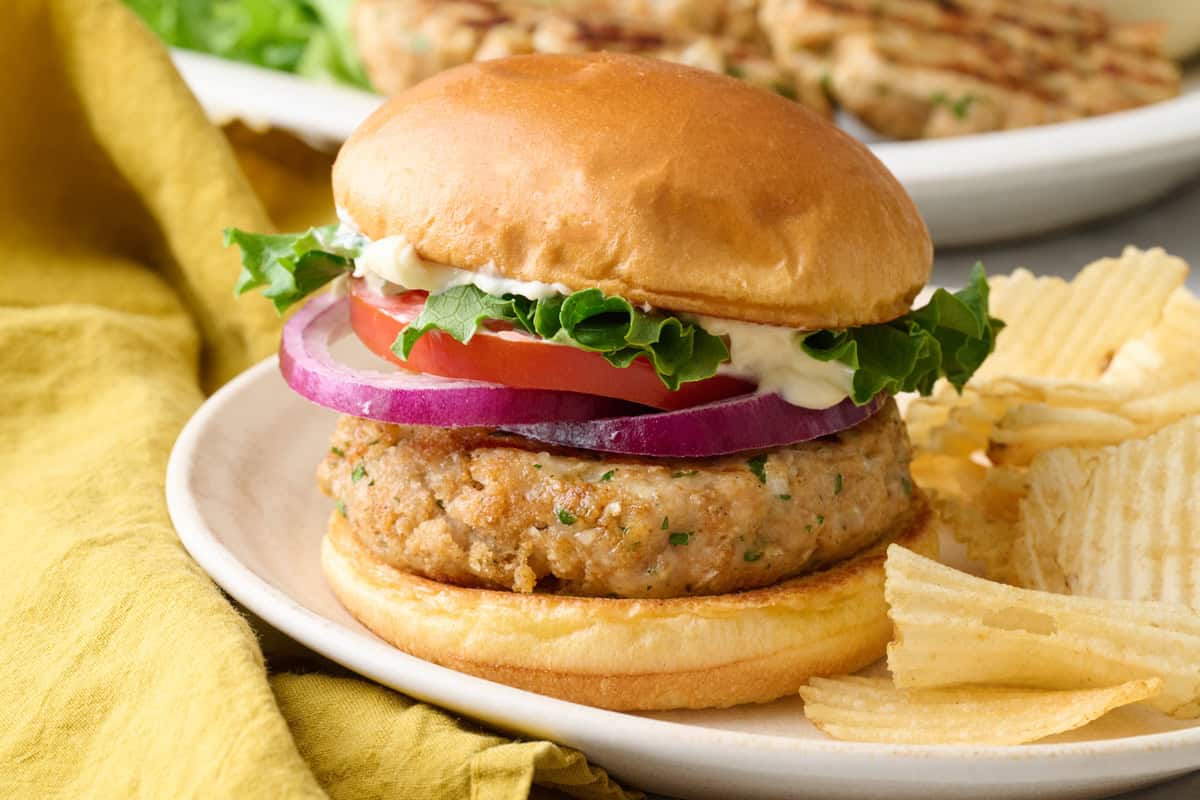 Easy ground chicken burger recipe on a bun with toppings and a side of chips.