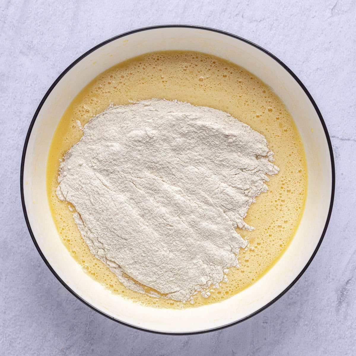 Egg mixture in a bowl with dry ingredients added on top.