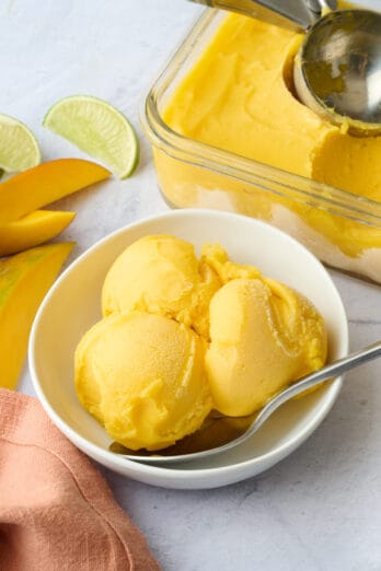 Easy mango sorbet scooped into a serving bowl with dish nearby.