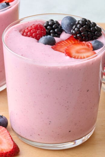 2 glasses of mixed berry smoothie topped with extra mixed berries and more berries either in a dish nearby.