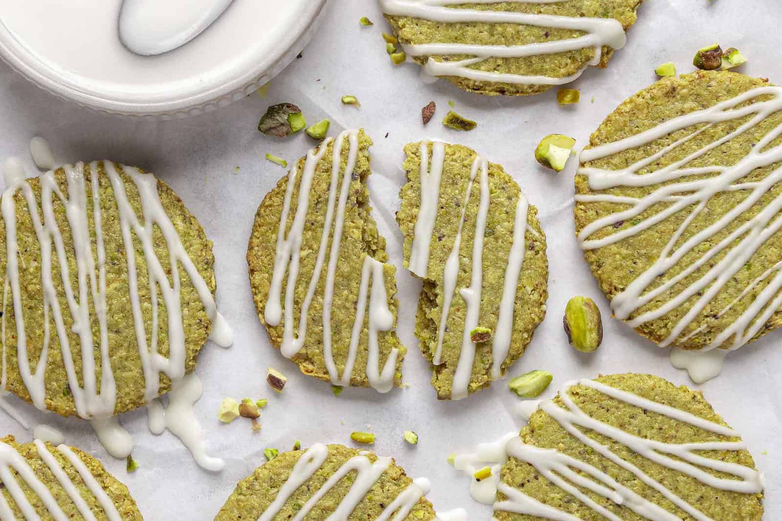 Easy pistachio cookies on parchment paper topped with white chocolate drizzle.