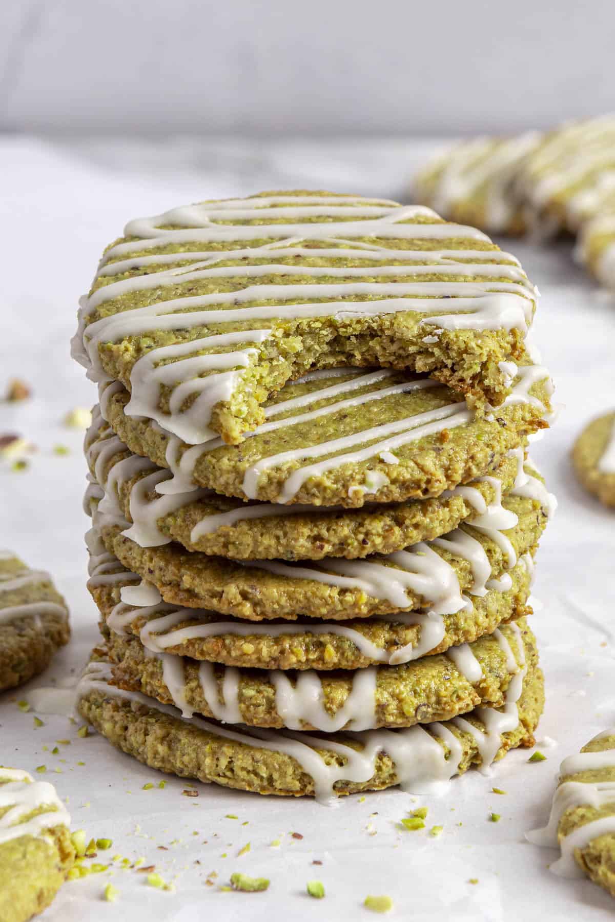 Stack of homemade pistachio cookies topped with icing and top cookie with a bite taken out.