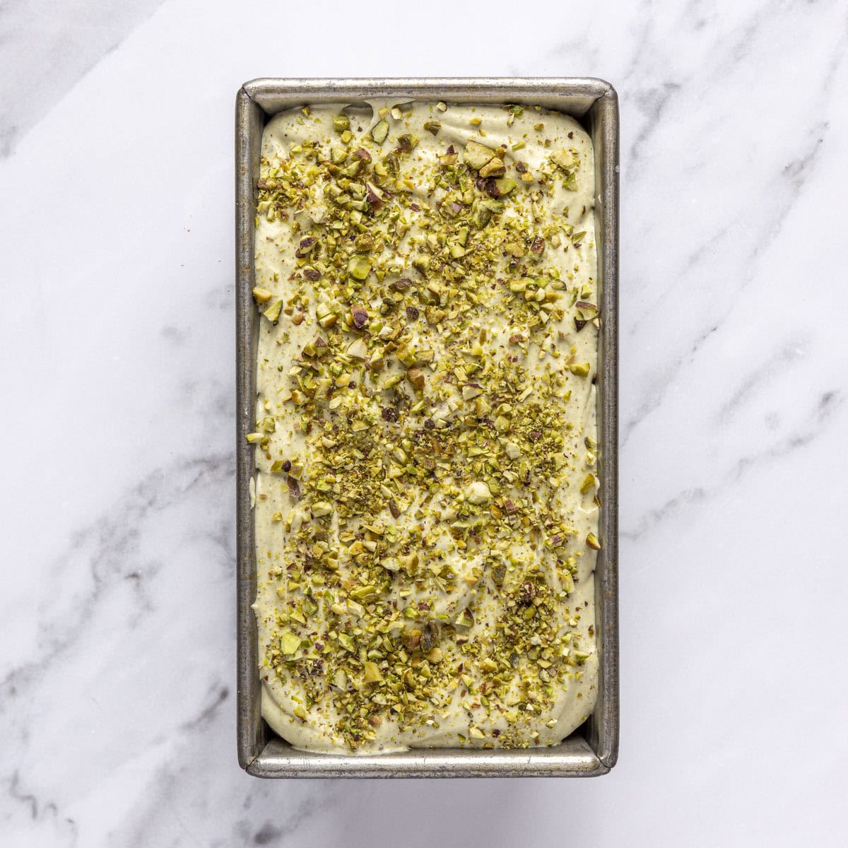 Pistachio ice cream in a freezer safe container topped with chopped pistachios.
