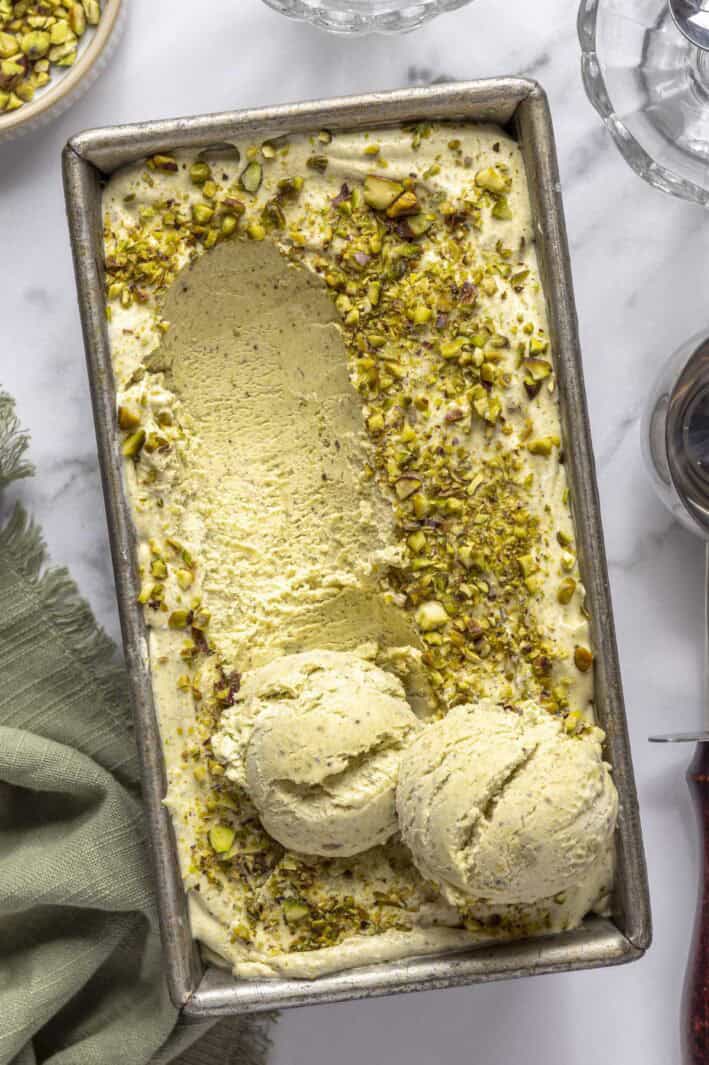 Easy pistachio ice cream recipe in a dish topped with chopped nuts and a few scoops of ice cream on top.