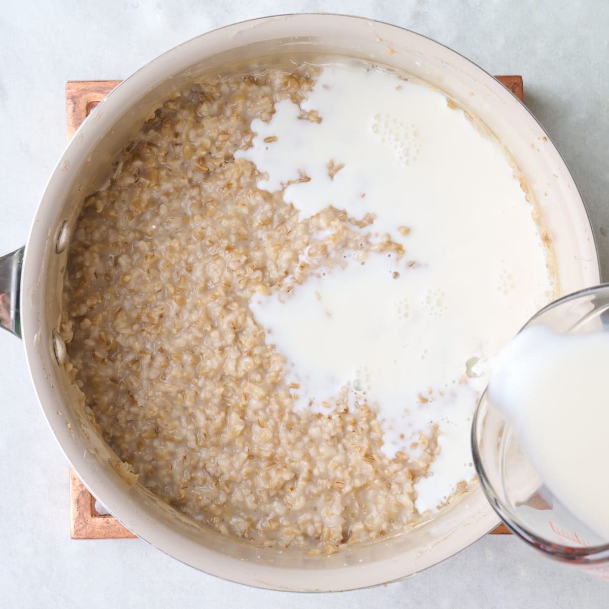 Milk being poured into pot with cooked oats.