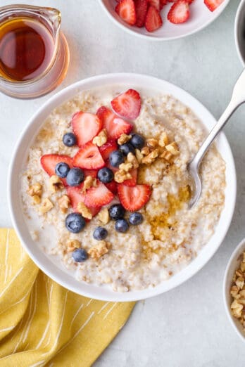 Bowl of steel cut oatmeal topped with blueberries, sliced strawberries, walnuts and maple syrup.