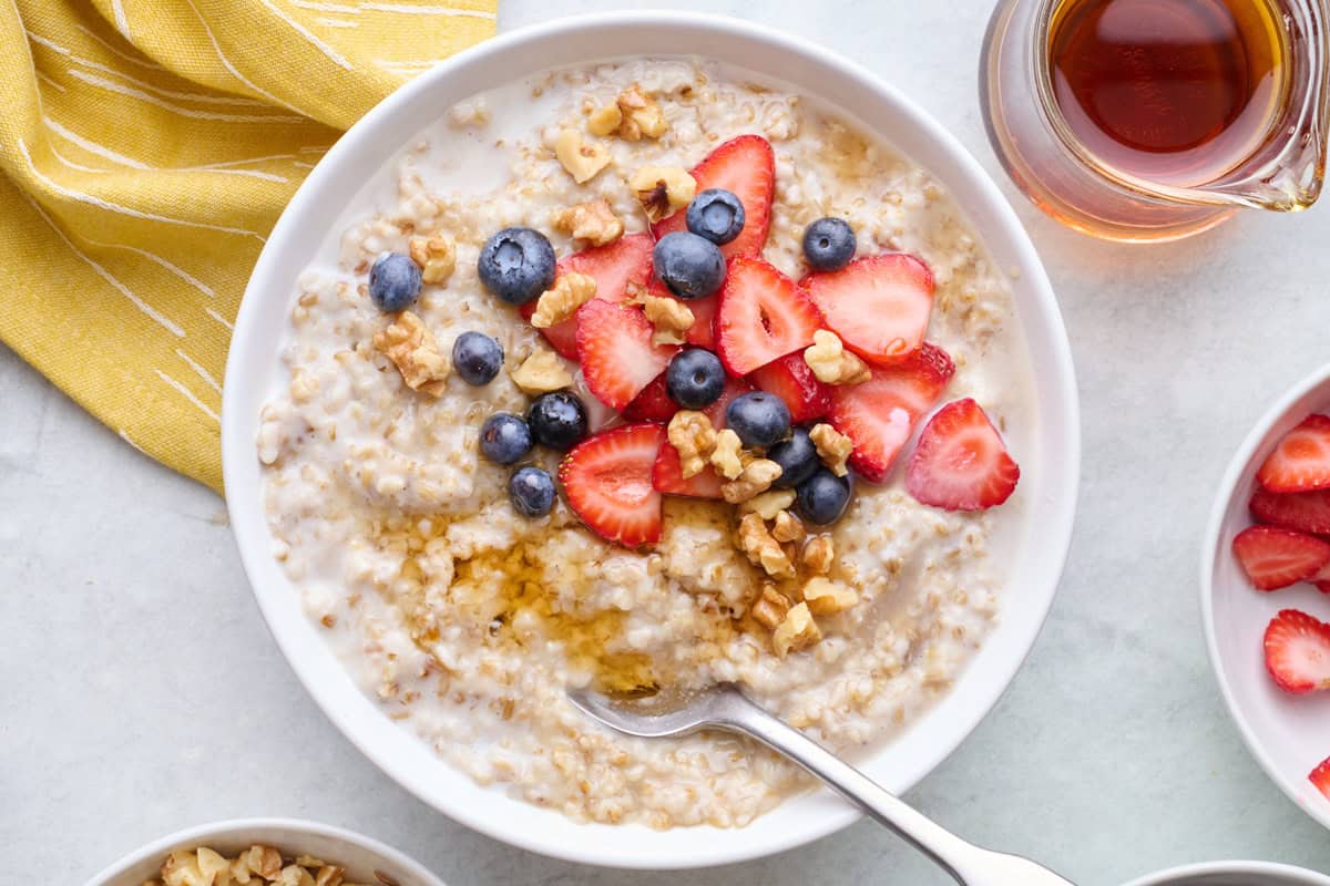 Bowl of steel cut oatmeal topped with blueberries, sliced strawberries, walnuts and maple syrup.