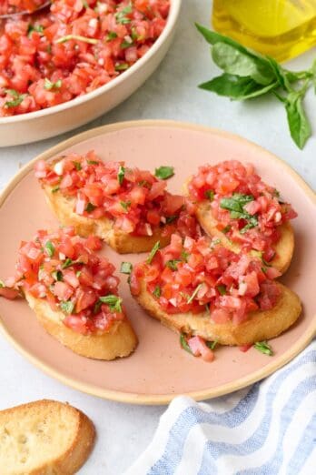 Tomato basil bruschetta on a plate with a bowl of more tomato mixture nearby.